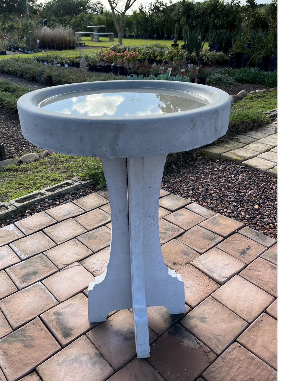 A cement birdbath on a paved patio